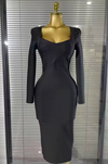A fitted black long-sleeve midi dress displayed on a gold dress form mannequin in front of window blinds.
