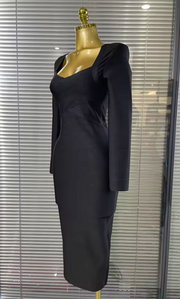 A black knee-length dress with a square neckline and long sleeves, displayed on a gold dress form mannequin in front of window blinds.