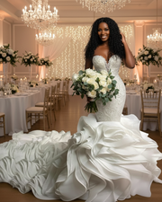 Luxurious strapless mermaid wedding dress featuring a deep sweetheart neckline, intricate beaded lace bodice, and a dramatic cascading ruffled train in elegant ivory satin.