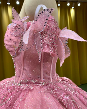Baby pink quinceañera gown with glitter details, lace trim, and full princess ball skirt.